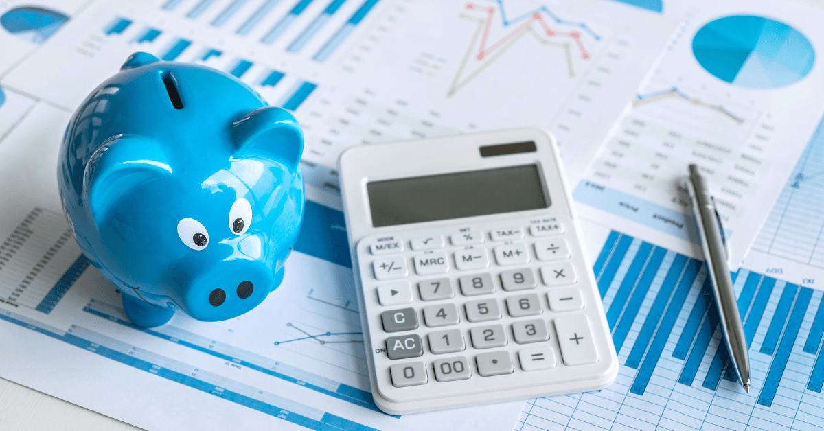 House and Land Packages -A calculator on a table with piggy bank and pen with graphs