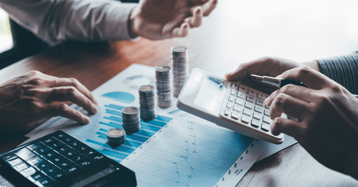 Passive Income Image 01 - Man holding a calculator and there are coins and another calculator along with a analysis sheet on the table, they are discussing about positive cash flow