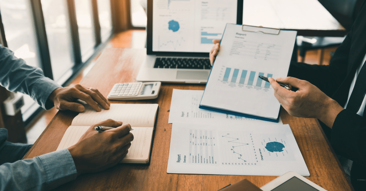building wealth through investment property - image of two persons pointing at a analytics and the other person is noting down and there is a laptop and calculator on the table