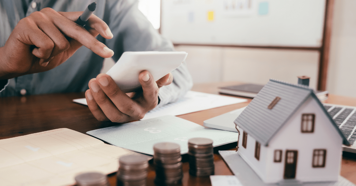 One of the Property investors calculating negative gearing risk on his calculator and there is a dummy house and some coins coins on the table
