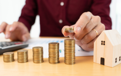 Person stacking coins next to a miniature house, symbolizing property investment and wealth building strategies related to financial freedom.